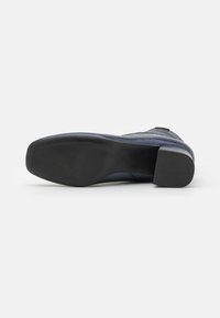 Zapato azul marino con parte superior lisa, pequeño tacón y suela de goma negra texturizada. Presenta una puntera redonda y mínimos acentos de metal.