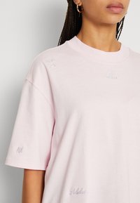 Ljust rosa oversized t-shirt i bomull, med broderade logotyper på bröstet och ärmarna, rund halsringning och korta ärmar.