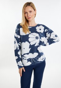 Marineblauwe trui met een wit bloemenpatroon, gestructureerde stof, brede mouwen en een ronde halslijn. Gecombineerd met marineblauwe broek.