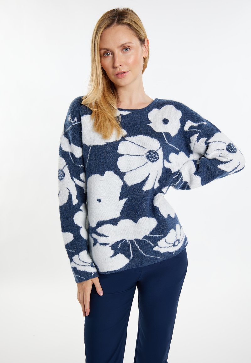 Marineblauwe trui met een wit bloemenpatroon, gestructureerde stof, brede mouwen en een ronde halslijn. Gecombineerd met marineblauwe broek.