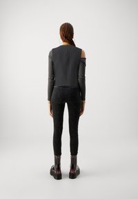 Top negro corto con mangas largas; leggings negros de cintura alta con un patrón texturizado; botas de tobillo brillantes con suela gruesa y cremallera.