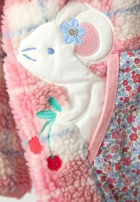 Material fuzzy roz, cu un șoarece brodat alb, înconjurat de o floare albastră și cireșe, completat de un textile cu model floral pe lateral.