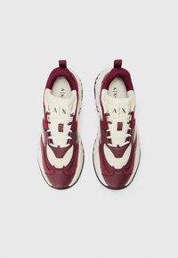 Des baskets de sport bordeaux et crème présentent des matériaux en mesh et en cuir, une semelle épaisse, des lacets ronds et un logo sur la languette.