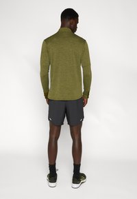 Cămașă sport cu mânecă lungă, de culoare verde măsliniu, cu guler, asortată cu pantaloni scurți negri. Caracteristici: material neted și design ajustat.