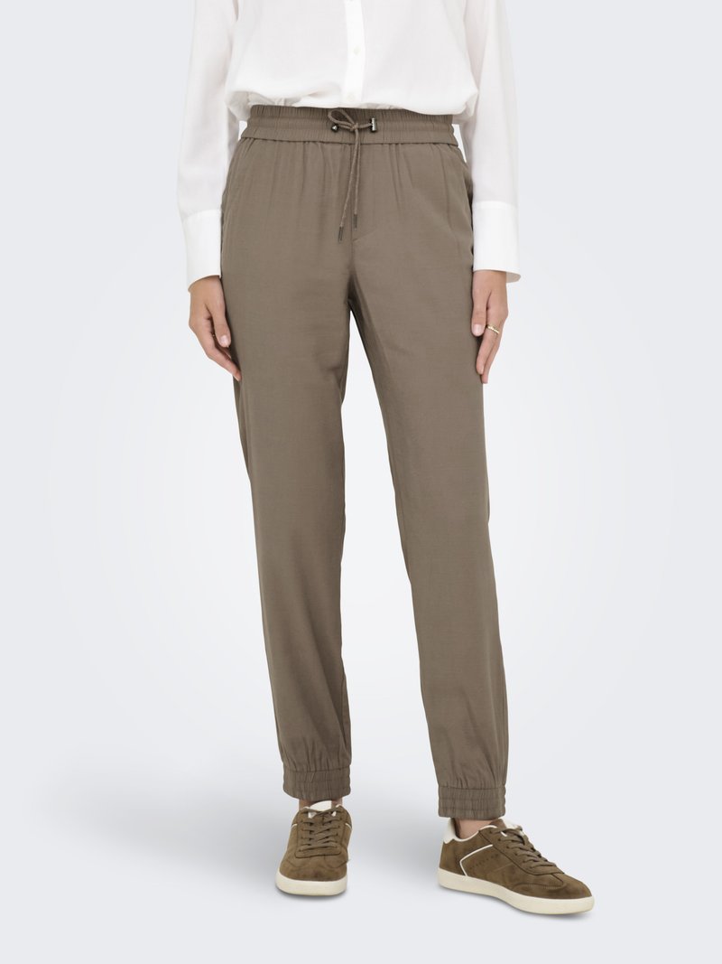 Pantalons joggers kaki avec taille élastique et cordon de serrage, présentant des jambes ajustées et des poignets élastiques. Portés avec des baskets en daim marron.