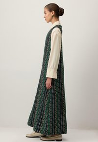 Rochie lungă, cu un model geometric, în nuanțe de verde și negru, cu o siluetă fluidă. Purțată peste o bluză de culoare deschisă.