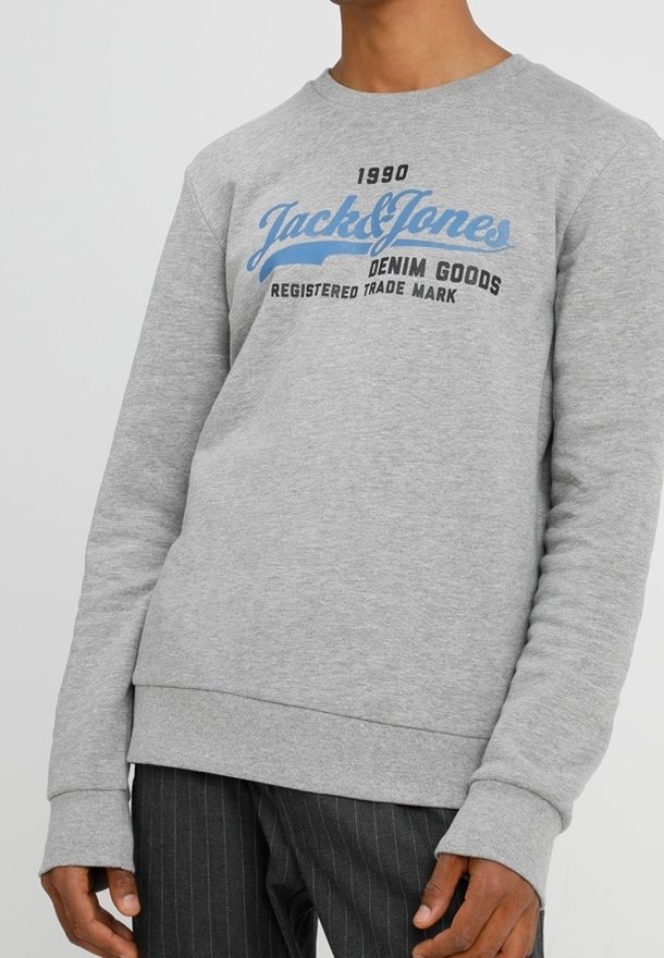 Hombre vestido con un sudadera de color gris claro que lleva el texto "1990 Jack & Jones Denim Goods Registered Trade Mark" en azul y negro en el pecho.