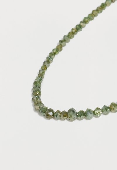 Κολιέ με χάντρες από πράσινες πολύγωνες πολύτιμες πέτρες, τοποθετημένο σε καμπυλωτή γραμμή σε λευκό φόντο.