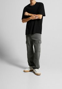 Černé oversized tričko s kulatým výstřihem, kombinované se světle šedými cargo kalhotami s bočními kapsami. Doplněno o bílé tenisky s gumovou podrážkou.