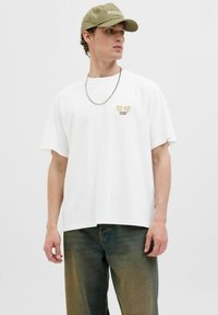 Hvid kortærmet T-shirt med afslappet pasform, der har et lille flerfarvet grafik på brystet og et tekstureret sølvkæde. 