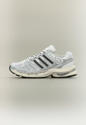 Baskets sportives blanches et grises avec des rayures noires, tige en mesh, semelle amortie et lacets, présentées de profil sur un fond neutre.