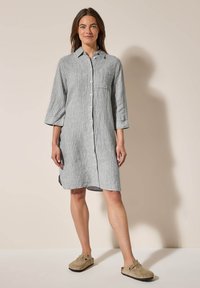 Abito camicia in lino grigio a righe con bottoni frontali, maniche lunghe e spacchi laterali. Presenta una tasca sul petto e polsini a contrasto.