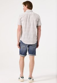 Korte mouwen overhemd met knopen in lichte stof met een wit en grijs bloemenpatroon, gecombineerd met blauwe opgerolde denim shorts en witte sneakers.