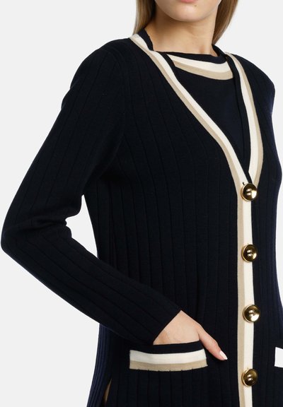 Marinblå ribbad cardigan med V-hals, krämfärgade ränder, guldknappar och sidofickor med en mjuk textur.