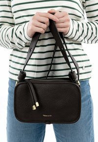 Brun läder crossbody-väska med en texturerad yta, detaljer i guld, och dragkedjestängning, hålls av en person i en randig topp.