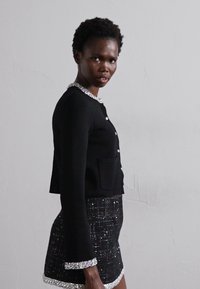 Svart stickad cardigan med silverdetaljer runt kragen, ihop med en svart och silver tweed kortkjol med rutmönster.