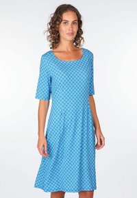 Blaudessin mit kurzen Ärmeln, quadratischem Ausschnitt, einem schwingenden Rock und einem sich wiederholenden geometrischen Muster in dunklerem Blau und Weiß.