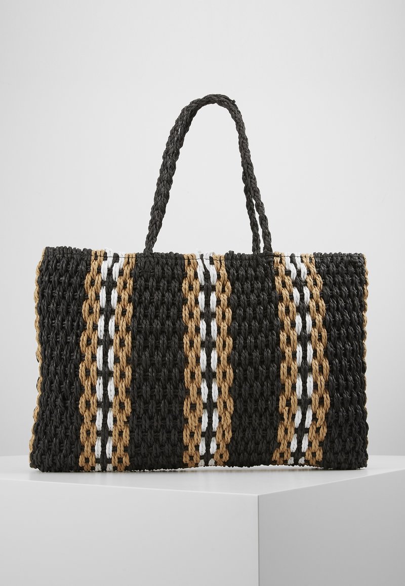 Woven tote bag o prostokątnym kształcie, z czarnymi, brązowymi i białymi paskami, teksturowaną powierzchnią oraz dwiema plecionymi rączkami.