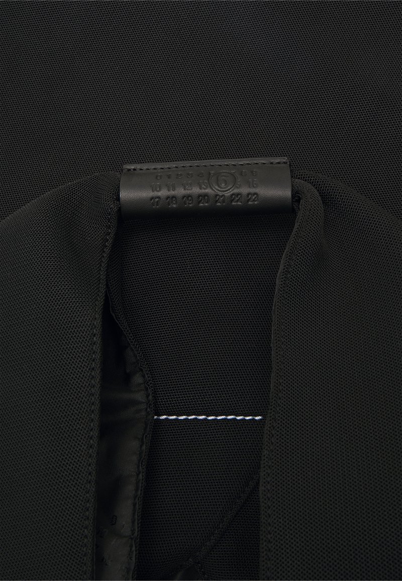 Tela de malla negra con un interior suave y una etiqueta negra texturizada que presenta los números del 0 al 22, costuras cosidas y un acento de hilo blanco.