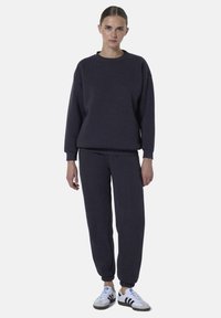 Donkergrijze sweatshirt en bijpassende joggingbroek van zachte stof, met een relaxte pasvorm, geribbelde manchetten en witte sneakers met zwarte strepen.