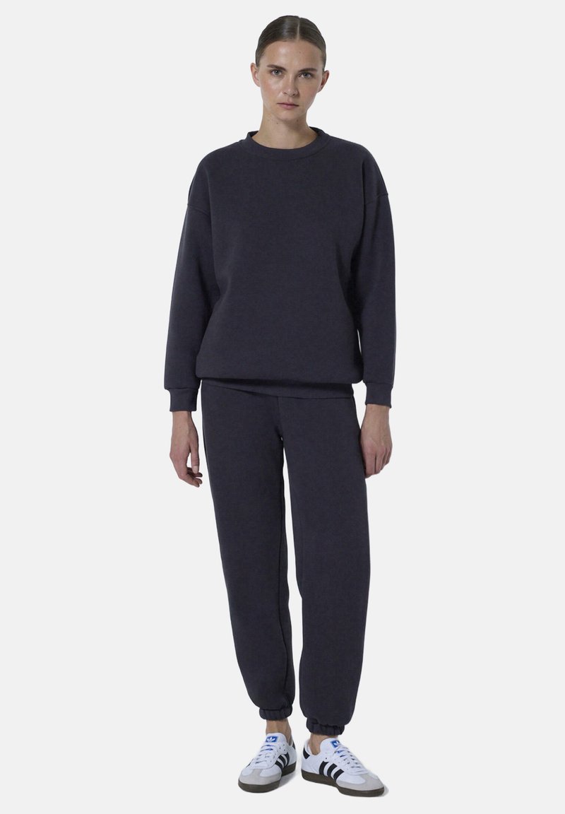 Donkergrijze sweatshirt en bijpassende joggingbroek van zachte stof, met een relaxte pasvorm, geribbelde manchetten en witte sneakers met zwarte strepen.