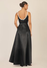 Langes schwarzes Satinabendkleid mit tiefem Rückenausschnitt und verziertem Ausschnitt. Der ausgestellte Rock sorgt für eine elegante Silhouette.