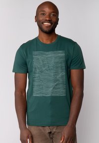 Groene katoenen t-shirt met een witte lineaire handgrafiek op de voorkant. Korte mouwen en een ronde hals. Zachte textuur.