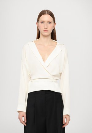 Weißes Wickelbluse mit langen Ärmeln, tiefem V-Ausschnitt und tailliertem Design. Weicher Stoff mit glatter Textur, kombiniert mit hoch taillierten schwarzen Hosen.