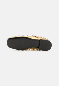 Scarpa dorata con suola nera, caratterizzata da una finitura metallica liscia, borchie decorative lungo il bordo e design a punta arrotondata.