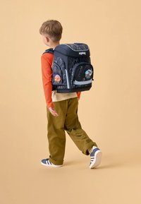 Zaino nero con motivo a fulmine, tasca frontale, striscia riflettente e toppe grafiche circolari. Stile di trasporto con spallacci regolabili.