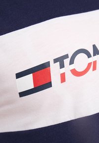 Navy and white striped T-shirt with a red and blue logo, featuring a smooth cotton texture and bold graphic detailing.