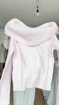 Hellrosa Pullover mit einem Schlauchkragen, weicher Strickstruktur, langen Ärmeln und geripptem Saum. Der Stoff wirkt gemütlich und lässig.