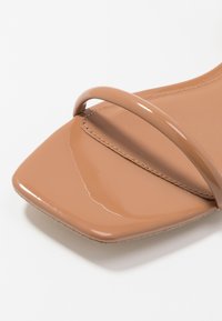 Nude patenttijahuripohjaiset sandaalit, joissa on neliömäinen varvas, kaksi kapeaa hihnaa ja sileä, kiiltävä pinta. Minimalistinen muotoilu, litteä pohja.