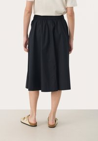 Zwarte, knie-lange rok met een elastische tailleband van een zachte, lichte stof. Draag met lichtgekleurde instap sandalen.