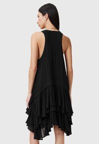 Vestido negro sin mangas con volantes en capas en el dobladillo, que presenta un corte relajado y una textura suave. La vista trasera resalta el escote curvado.