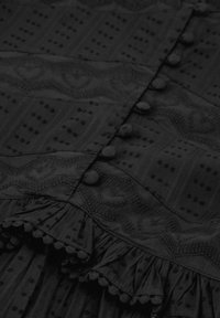 Zwarte jurkstof met textuurpatronen, voorzien van knopen, een rucheszoom en decoratieve rand. Details omvatten hart- en stipmotieven.