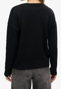 Suéter negro de punto con dobladillo acanalado, con hombros caídos y un corte relajado. Combinado con jeans grises, ligeramente desgastados.