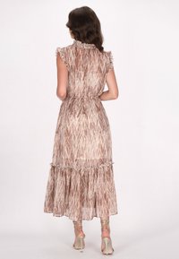 Maxi-Kleid in hellbeige mit braunen abstrakten Mustern. Verfügt über Rüschenträger, eine taillierte Taille und einen mehrlagigen Rock. Kombiniert mit metallischen Absätzen.