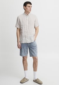Világos bézs rövid ujjú ing, farmer sort, fehér térdzokni, bézs slip-on cipő. Lazac outfit kényelmes szabással és minimalista részletekkel.