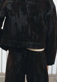 Jachetă din catifea neagră cu o suprafață texturată, având o croială scurtă și o pereche asortată de pantaloni cu buzunare aplicate.