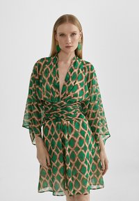 Zelena haljina sa uzorkom i kimono rukavima, s naglašenim strukom i apstraktnim dizajnom dijamanata u nijansama smeđe i zelene.