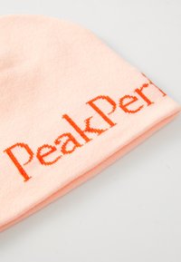 Light pink knit beanie hat featuring the text "Peak Performance" in bold orange stitching. Soft fabric with a fitted, tapered shape.