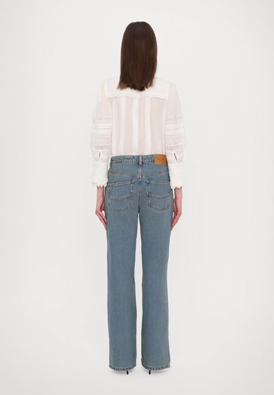 Lichte denim high-waisted jeans met een rechte pijp, voorzien van achterzakken en een leren patch op de tailleband. Vooraanzicht wordt bedekt door een top.