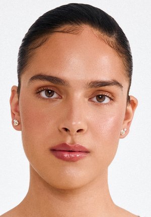 Naisest lähivaade, kellel on siledad nahk, tahutud mustad juuksed, loomulik meik, läikivad huuled ja väiksed pärlikõrvarõngad mõlemas kõrvas.