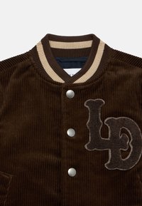 Καφέ τζάκετ από κορντόρι με ριμπ κολάρο, ασημένια κουμπιά πίεσης και κεντημένο λογότυπο "LD" στο μπροστινό μέρος.