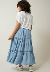 Falda maxi azul claro, con volantes y cintura fruncida, combinada con una camiseta blanca casual y zapatillas blancas.