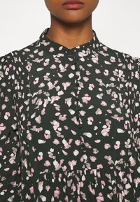 Robe vert foncé avec un motif dispersé à pois roses et blancs, dotée d'un devant boutonné, d'un col montant et d'un détail froncé à la taille.