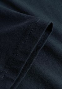 Κοντινή λήψη σκούρου μπλε υφάσματος που δείχνει διπλωμένο τελείωμα με τακτικές, ομοιόμορφα τοποθετημένες ραφές.
