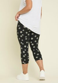Svarta caprileggings med ett livfullt prästkrage-mönster. Kombinationen med en vit skjorta och vita sneakers framhäver de blommiga detaljerna och passformen.
