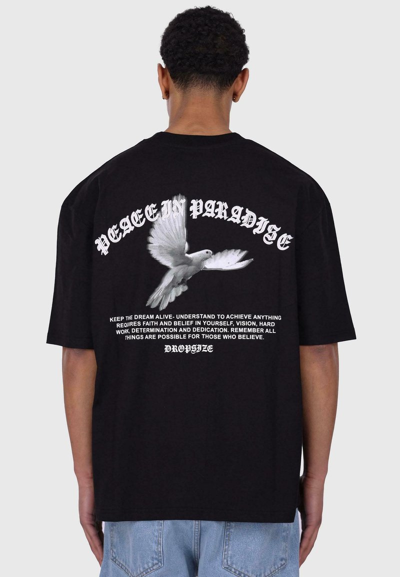 Svart bomulls t-skjorte med et hvitt duegrafikk og teksten "PEACE IN PARADISE" på baksiden, med ekstra motiverende tekst under.